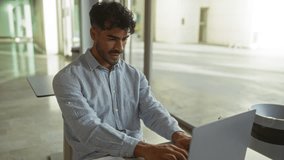 Young man working on laptop in modern office with sunlight streaming through large windows, appearing excited and smiling while typing on keyboard, wearing casual shirt and relaxed. - Powered by Shutterstock - Get 15% off with code: PIKWIZARD15