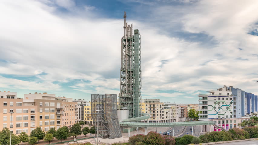 Timelapse hyperlapse of old steel refinery tower with spiral ramp in Lisbon's Park of Nations modern district. Traffic and cloudy sky in the background. Apartment buildings around. Portugal