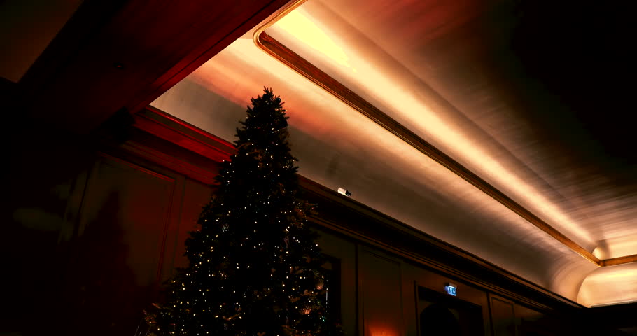 A warmly lit interior featuring a tall Christmas tree adorned with lights, set against a backdrop of luxurious wood panels and gold accents.