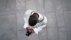 Young Black man in stylish attire types message on smartphone screen while standing on city sidewalk.Focus on mobile device and digital communication. Dark skinned male chatting online in social media - Powered by Shutterstock - Get 15% off with code: PIKWIZARD15