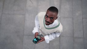 young Black man in stylish clothing enjoys using his smartphone while standing outdoors. blurred screen suggests social media use, messaging, or browsing, highlighting modern digital connectivity - Powered by Shutterstock - Get 15% off with code: PIKWIZARD15