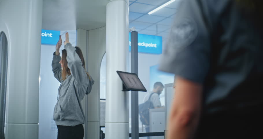 Security Checkpoint in Airport Terminal: Young Woman Stands in X-ray Human Body Scanner. Rack Focus on Female TSA Worker Wearing Uniform with Airport Security Logo Patch on the Sleeve. Close Up.