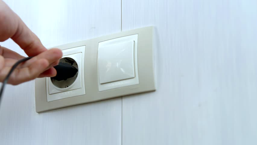 Puts Power Plug In Wall Socket. Electrical Appliances Equipment. Inserts Plug Into Electrical Socket. Plugging Charger Cable To Electrical Power Point. Energy Saving Connect Plug To Wall Outlet Socket