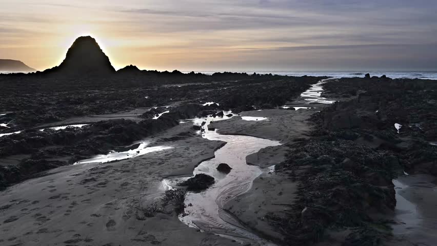 Sun setting behing large rock on Widemouth Bay Cornwall