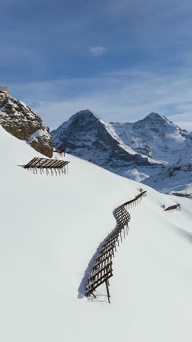 Eiger North Face and Monch Mountains in Winter. Swiss Alps. Switzerland. Aerial View. Moving Forward and Upwards over Mannlichen. Reveal Shot. Anti-Avalanche Structures. Vertical Video