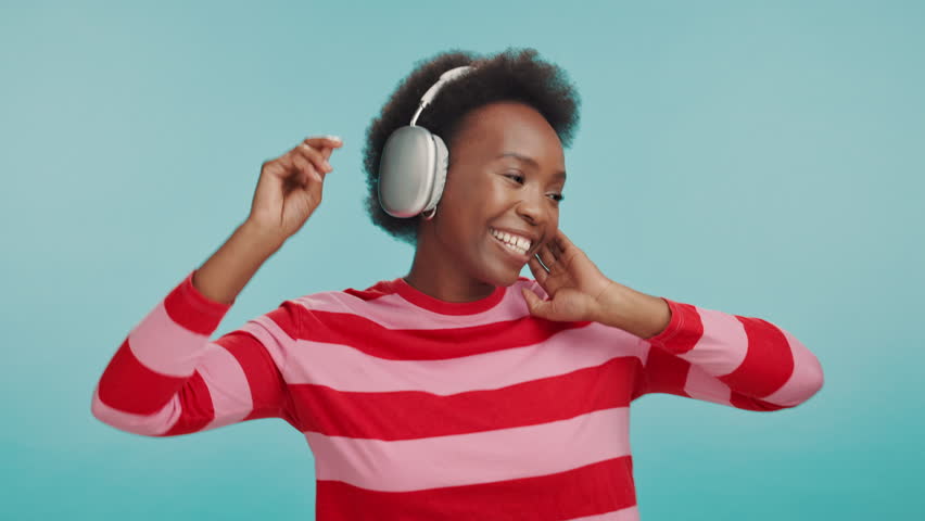 Black woman, happy or dancing with headphones in studio for hip hop track, energy or song album. Freedom, dancer or party movement with radio app, celebration or streaming service on blue background