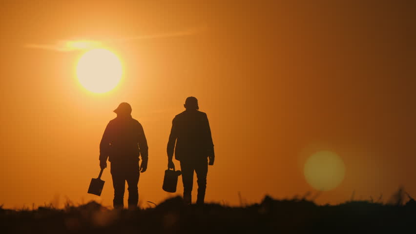 Silhouettes of two farmers walking through a vast open field during a vibrant golden sunset, carrying essential tools like a watering can and a shovel, embodying rural life and hard work