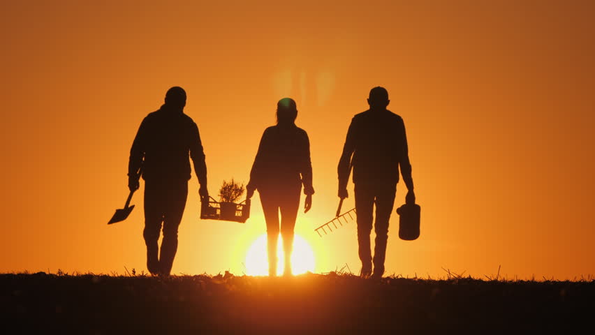 A silhouette of a farmer walking across a field during sunset, holding a spade and a bucket. The warm golden light creates a dramatic and serene rural scene. 
