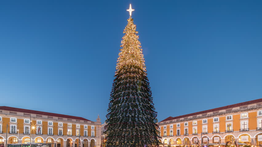 Commerce Square in Lisbon illuminated at Christmas day to night transition hyperlapse, with a towering tree and crowds celebrating. Timelapse of the festive atmosphere and historic architecture