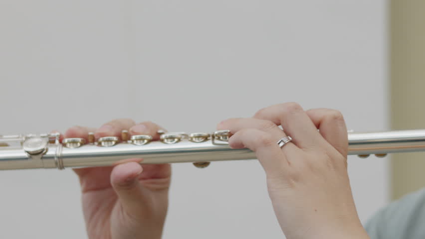 Hands play a polished silver flute, emphasizing the artistry and finesse of musical performance. The close-up captures details of the instrument and passion, and dedication to classical music.
