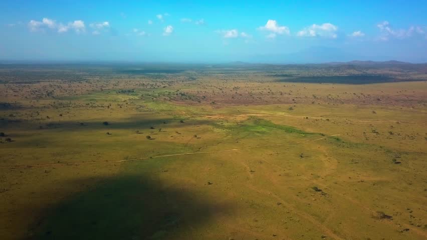 Vast savanna landscape featuring sparse vegetation and cloud shadows in Kidepo Valley National Park, showcasing the breathtaking wilderness of northeastern Uganda, drone dolly in shot