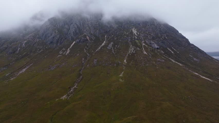 Aerial drone footage of the Glencoe mountain range in the Scottish Highlands, taken in summer on a clear but misty day, morning time.