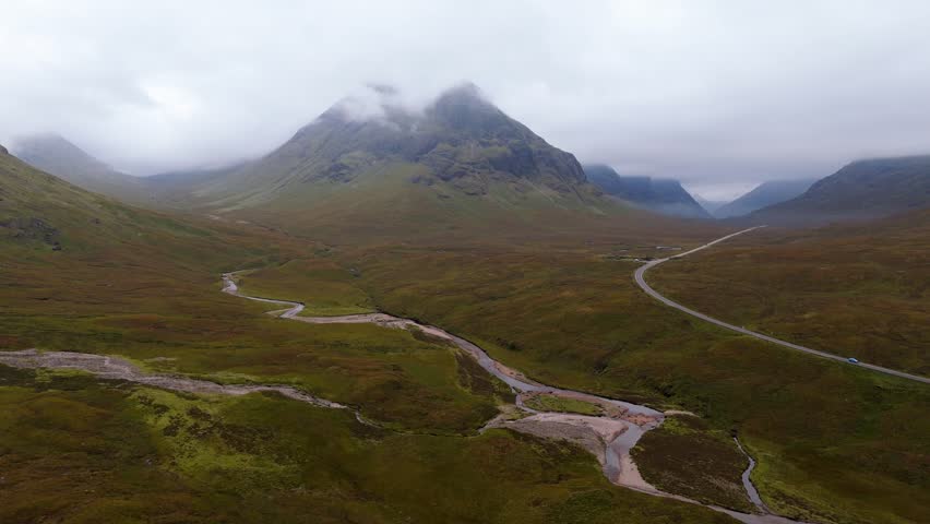 Aerial drone footage of the Glencoe mountain range in the Scottish Highlands, taken in summer on a clear but misty day, morning time.