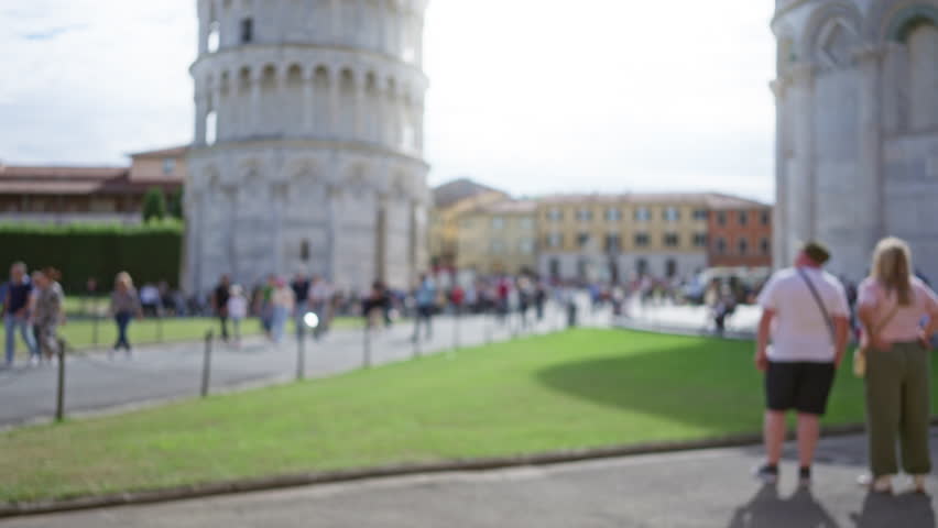 Blurry view of people near leaning tower in pisa capturing vibrant italian atmosphere with lush greenery and iconic architecture showcasing famous monument and bustling tourist scene