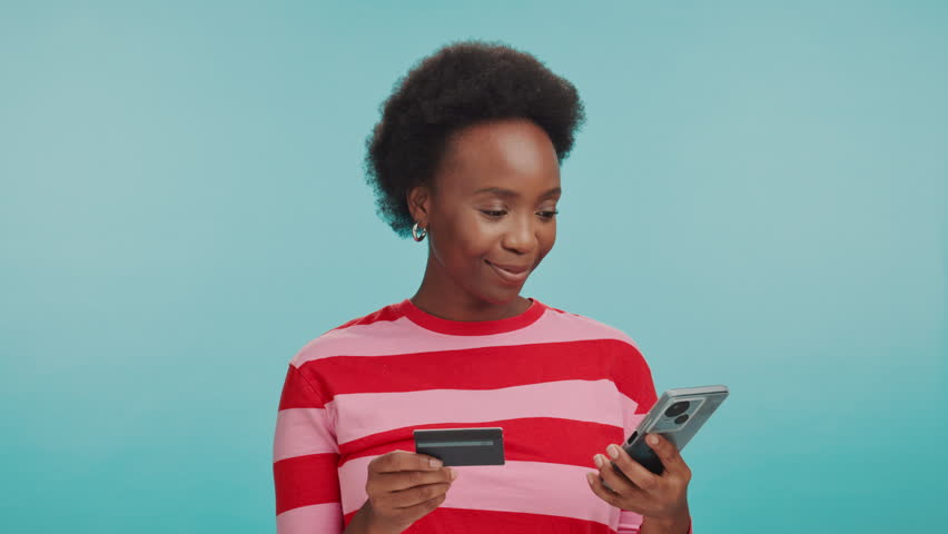 Black woman, mobile and credit card in studio for online shopping, trading and website registration. Customer, phone or bank app on blue background for ecommerce, payment or happy for retail promo