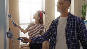 Man and woman painting walls together in a bright living room, sharing a joyful moment during home renovation, embodying teamwork and creativity in their new apartment. - Powered by Shutterstock - Get 15% off with code: PIKWIZARD15