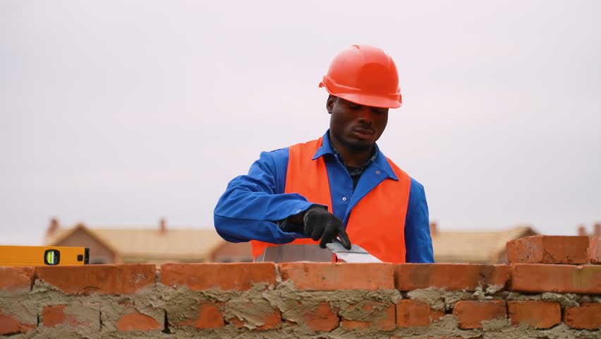 African American builder laying bricks at cottage construction site