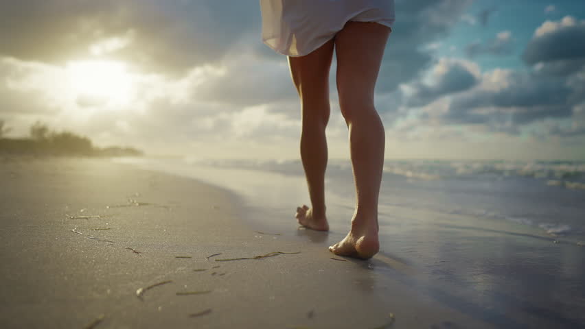 Enjoy solitude and unity with nature, woman legs on sandy shore, lady walking. Rearview of sexy female person strolling alone in sunset on coastline, barefoot vacationer feeling warm water and sand