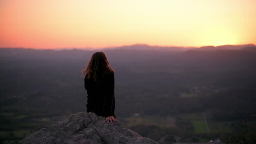 Woman Watching Serene Sunset at Buffalo Mountain Park woman sits on rocky ledge overlooking vast landscape at sunset in Buffalo Mountain Park, Tennessee, enjoying peaceful moment and scenic view
