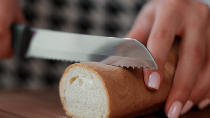 Woman slicing fresh bread with a serrated knife, Close-up of a hand using a serrated knife to slice fresh bread.