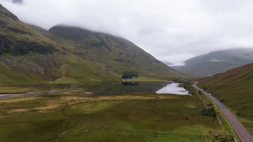 Aerial drone footage of Loch Achtriochtan in the Glencoe mountain range in the Scottish Highlands, taken in summer on a clear but misty day, morning time.