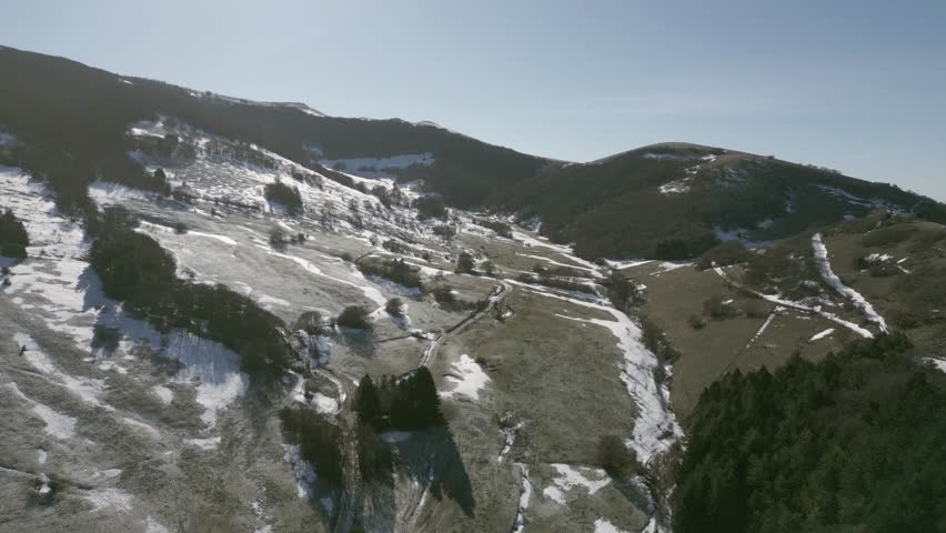 Drone view over Valsorda, Gualdo Tadino, on a sunny winter day. Snow-dusted peaks rise above a vibrant landscape, blending crisp white and rich earthy tones under a clear blue sky
