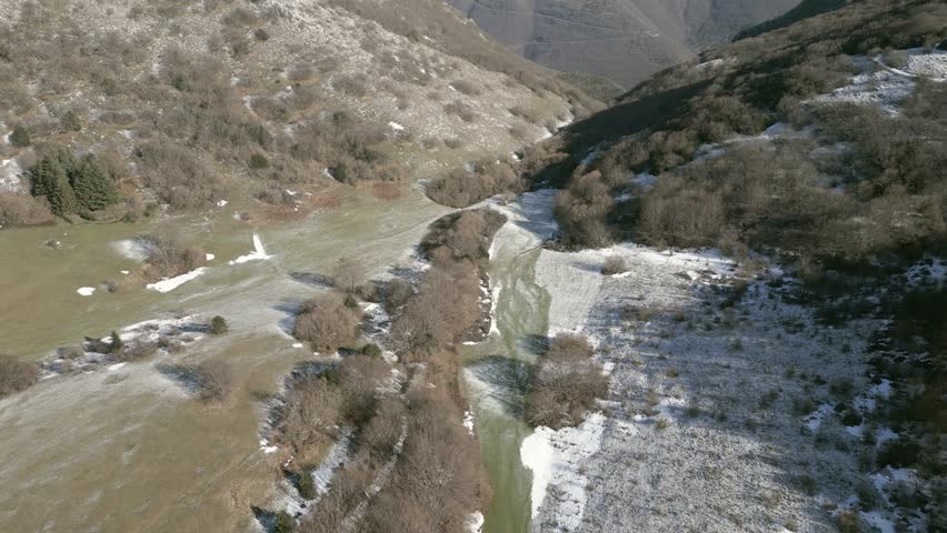 Drone view over Valsorda, Gualdo Tadino, on a sunny winter day. Snow-dusted peaks rise above a vibrant landscape, blending crisp white and rich earthy tones under a clear blue sky