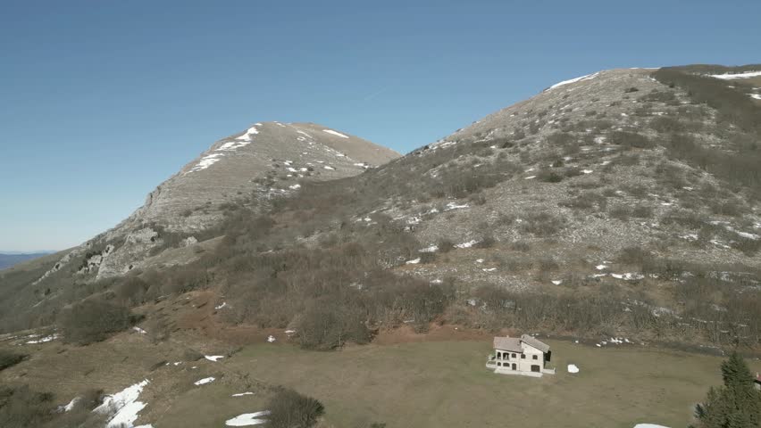 Drone view over Valsorda, Gualdo Tadino, on a sunny winter day. Snow-dusted peaks rise above a vibrant landscape, blending crisp white and rich earthy tones under a clear blue sky