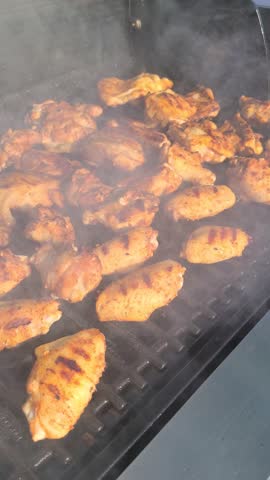 Chicken wings sizzling and smoking on top of a fire grill during a sunny summer day.