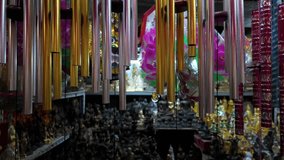 Close-up shot of metallic wind chimes swaying in a dimly lit Buddhist souvenir shop. The hanging chimes, in silver gold, and red tones shelves filled with golden Buddha statues and religious artifacts - Powered by Shutterstock - Get 15% off with code: PIKWIZARD15