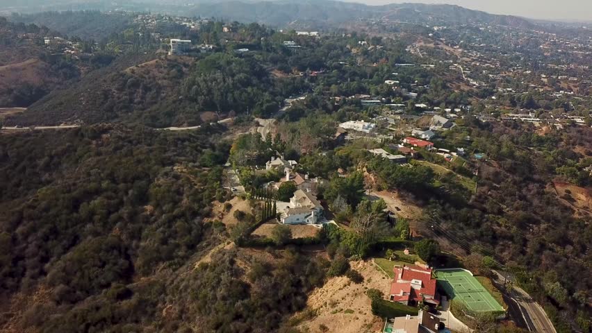 Swimming pool along upscale villas on top of american town. Aerial top down flyover. Sunset time in California. Noble mansions with forest landscape. Tennis Fields on top of mountain. Wide shot.