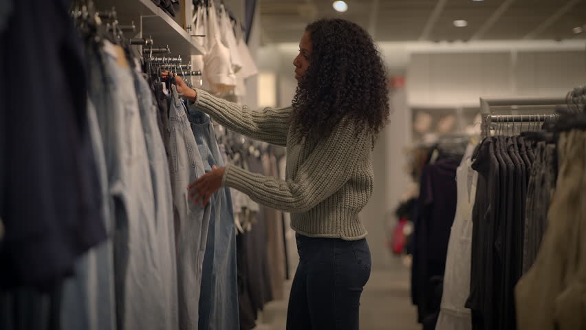 A woman is seen shopping for stylish clothes and accessories in a contemporary fashion retail store