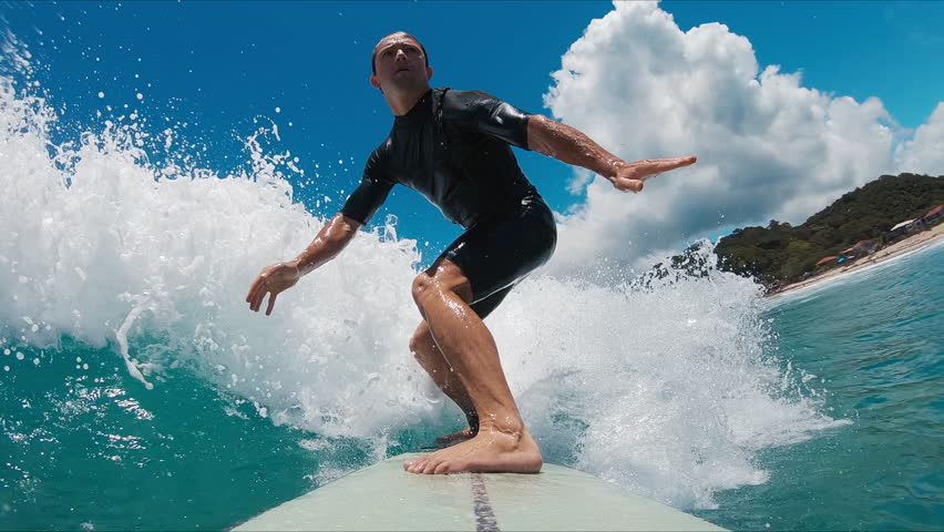 POV ocean surfing. Young male amateur surfer rides a wave and carves in a blue ocean
