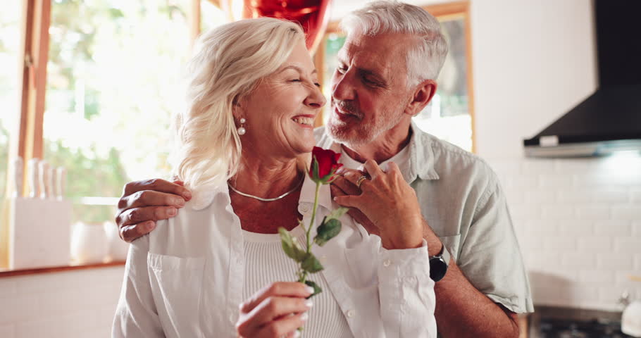 Love, senior couple and rose for valentines day, romantic gift and smile in kitchen. Retirement, man and woman with flower together for relationship, smell and kiss to celebrate marriage in home