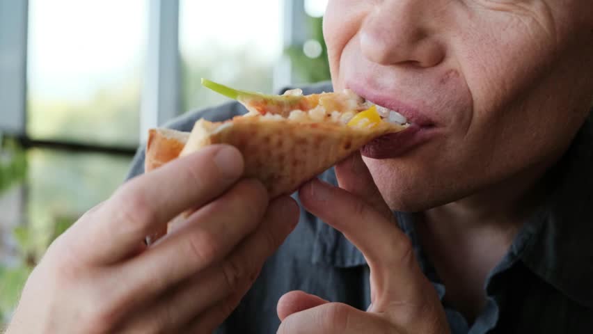 A man in a restaurant takes a slice of pizza from a plate and begins to bite off a piece. Perfect 4K video for food ads, restaurant promos, and culinary content.