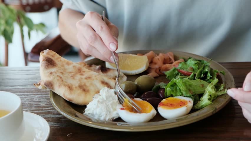 Close-up of a woman's hand with a fork gently taking the yolk from a poached egg on a plate. Perfect 4K video for food ads, restaurant promos, and culinary content.