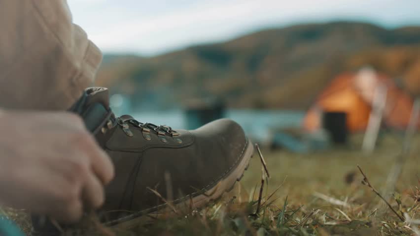 Human ties shoelaces against the background of nature. Adjust your hiking shoes on a sunny day. human tying shoelace on hiking boot, getting ready for hike at forest. Hiker tying shoes on hike.