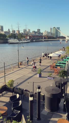Vertical video of Puerto Madero, Buenos Aires, Argentina at sunset. You can see the La Plata river, office buildings and people strolling