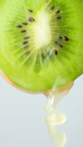 Kiwi juice running down half of fresh kiwi fruit, vertical slow motion macro.