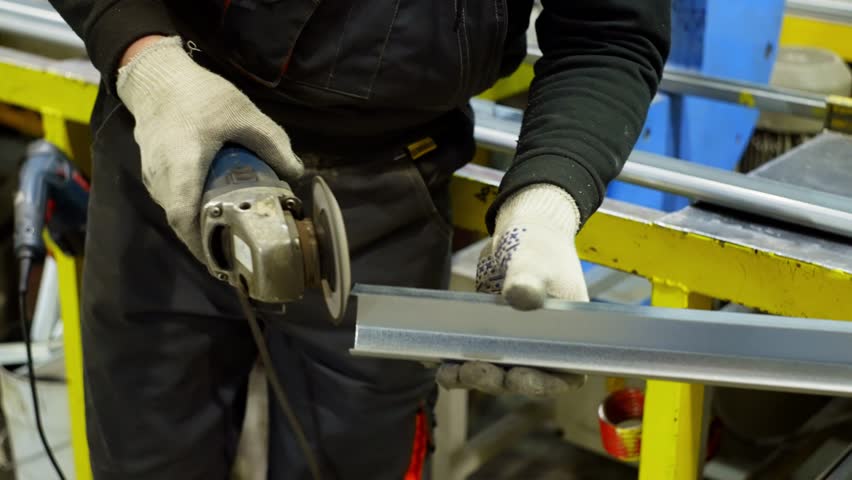 Industrial Engineer Grinding Metal Profile with Angle Grinder, Removing Burrs and Smoothing Edges for Precision Manufacturing in a Heavy-Duty Factory Workshop. High quality 4k footage