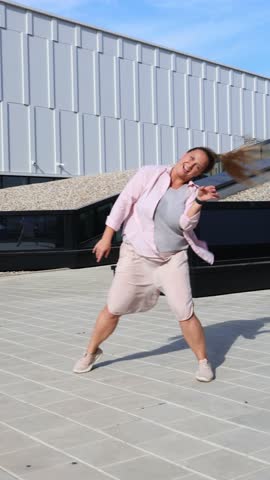 Confident Smiling Young Plus-Size Woman Dancing Outdoors in City, Joyful Curvy Female Shaking Hair with Energy and Positivity