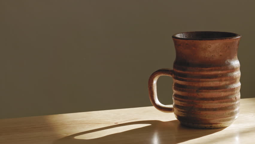 A person grabbing an old beautiful cup from the wooden table