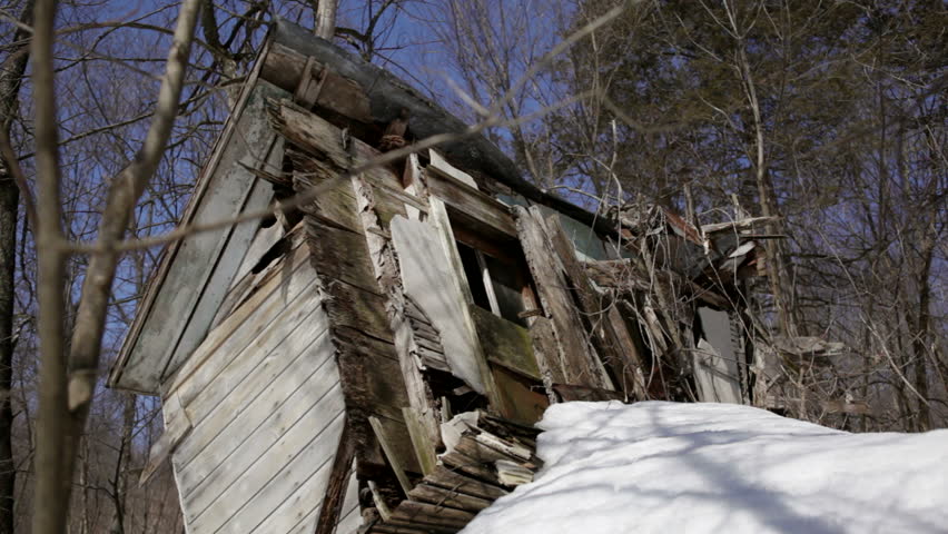 Abandoned 1910 homestead in a snowy forest in rural Wisconsin. The house is so weathered that the outer walls have collapsed and the roof lies next to it. Leaning porch featured. Midwestern USA.