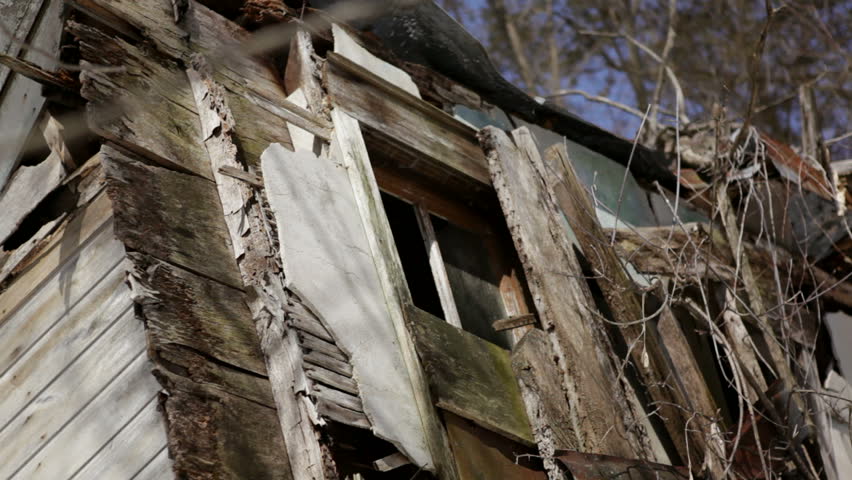 Abandoned 1910 homestead in a snowy forest in rural Wisconsin. The house is so weathered that the outer walls have collapsed and the roof lies next to it. Leaning porch featured. Midwestern USA.
