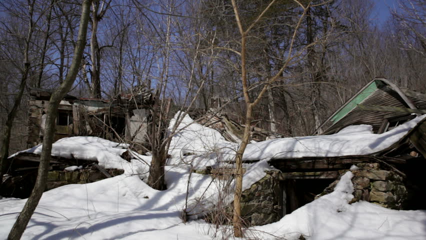 Abandoned 1910 homestead in a snowy forest in rural Wisconsin. The house is so weathered that the outer walls have collapsed and the roof lies next to it. Midwestern USA.
