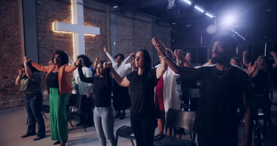 Congregation holding hands in unity, standing together during worship service, illuminated cross symbolizing faith and spirituality in a serene and inspirational atmosphere