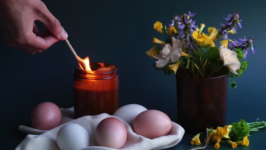 Easter holiday decorations. Easter concept background. 4K video. Cozy home-made easter composition with easter eggs, flowers and a lighted candle. Man lights the candle.