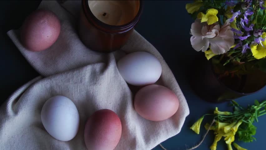 Top view of easter eggs with spring flowers, candle. Easter concept. Coloured eggs for Easter dinning. Rotation.
