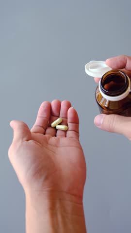 A close-up shot of hands pouring capsules from a brown medicine bottle into the palm