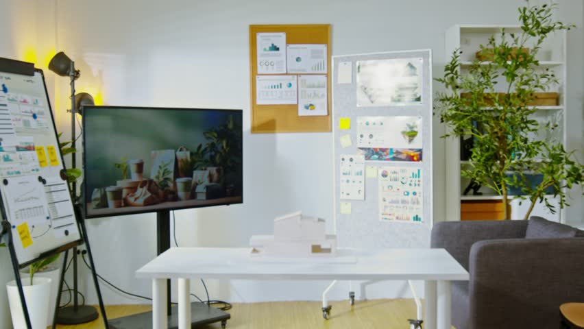 Modern office workspace with white desk, TV screen, presentation boards, indoor plants, and creative atmosphere showcasing productive and modern design elements for inspiring workspace.